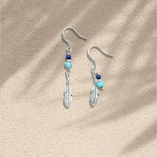 Silver feather dangle earrings with blue and turquoise beads on beige textured background