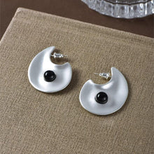 Pair of silver abstract-shaped stud earrings with black round accents on beige fabric