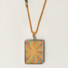 Colorful rectangular pendant with swirling orange, green, blue, and red pattern on gold braided necklace