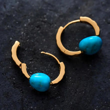 Gold hoop earrings with irregular turquoise stone accent on dark textured background