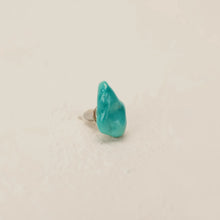 Close-up of a turquoise stone stud earring on a beige surface