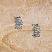 Silver stacked twig design stud earrings on textured beige surface