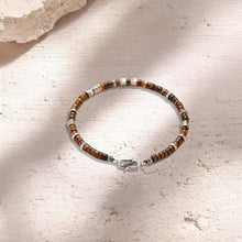 Beaded bracelet with brown and silver beads on textured light beige surface with stone