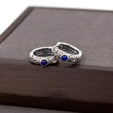 Pair of silver rings with blue stones and intricate swirling patterns on dark wooden surface