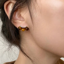 Close-up of ear wearing silver stud earrings with three small brown tiger eye beads