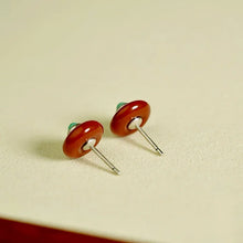 Close-up of round brown stud earrings with silver posts on beige surface