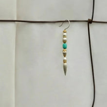 Single boho-style earring with white, gold, and turquoise beads hanging on rusty wire against plain white wall