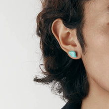 Close-up of ear wearing turquoise stone stud earring with black hair on white background
