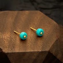 Gold stud earrings with round turquoise stones on a wooden hexagonal display