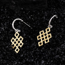 Silver and gold geometric dangle earrings with textured infinity knot design on black textured background