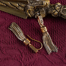 gold-tone metal tassel earrings with intricate chain link design on textured burgundy fabric