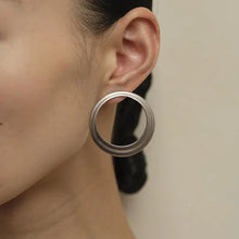 Close-up of ear with large silver hoop earring, minimalistic style on neutral background