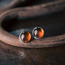 Pair of round amber stud earrings set in metal on rusty textured surface