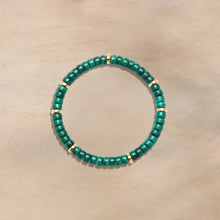 Green beaded bracelet with gold accents on beige background, stylish fashion accessory