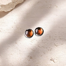 Pair of round amber stud earrings with silver backing on textured beige surface