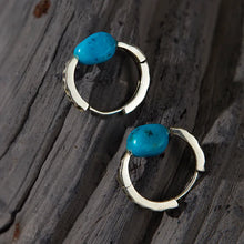 Silver hoop earrings with polished turquoise stones on rustic wooden background