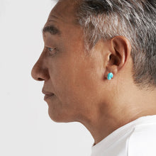 Side profile of elderly man with gray hair wearing turquoise stud earring and white shirt