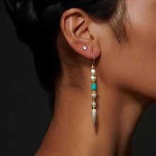 Close-up of a woman's ear wearing a long boho-style earring with white and turquoise beads and gold accents