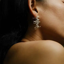 Close-up of a woman's ear wearing unique silver abstract wire earrings against dark background