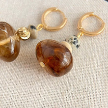 Close-up of stylish gold hoop earrings with amber glass and spotted stone beads on textured fabric