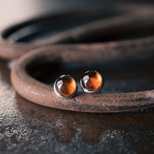 Close-up of polished brown amber stud earrings on rustic metal rings