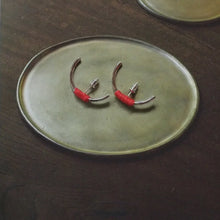 Silver hoop earrings with red thread wrap displayed on a green oval ceramic dish on a dark wooden surface