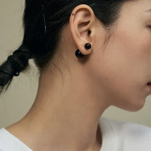 Close-up of a woman wearing black double ball stud earrings with hair tied back and white top