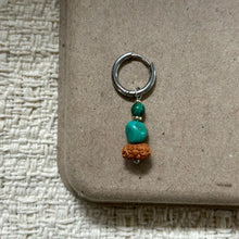 Silver hoop earring with green beads and natural brown seed pendant on textured beige surface