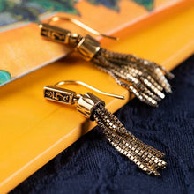 Close-up of elegant gold tassel earrings on yellow and dark blue fabric background