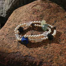 Double-strand pearl bracelet with multicolored raw gemstone beads on rustic stone surface