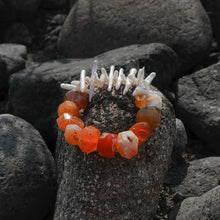 Handcrafted bracelet with orange agate and white pearl beads displayed on dark volcanic rocks