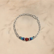 Silver chain bracelet with mixed blue and silver beads and one central red bead on beige background