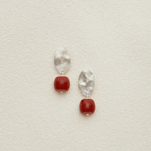 Silver fingerprint earrings with red rounded square beads on textured beige background