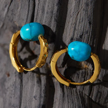 Gold hoop earrings with textured design and vibrant turquoise stone on rustic wood background