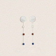 Minimalist drop earrings with white, red, and blue beads on a textured beige background