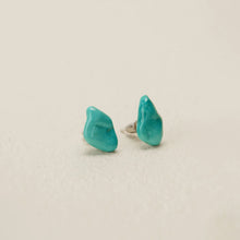 Close-up of natural turquoise stud earrings with silver posts on beige background