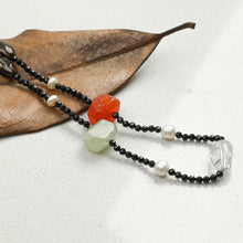 Black beaded necklace with pearls, orange and green stones on a dry brown leaf