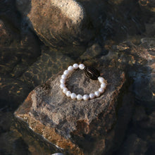 Pearl bracelet with black stone centerpiece on a wet rocky surface in natural light