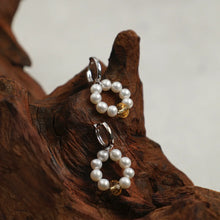 Pearl hoop earrings with golden crystal bead displayed on textured brown wood