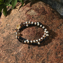 Beaded bracelet with white pearls and black beads on textured brown stone surface with green leaves