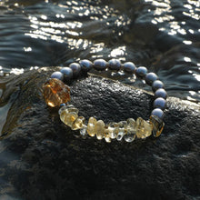 Elegant bracelet with golden and translucent stones and dark pearls on wet black rock by water
