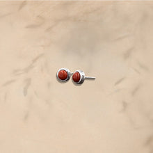 Silver stud earrings with round red gemstone on beige background