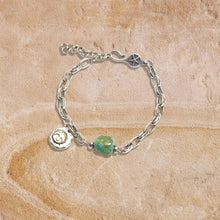 Silver chain bracelet with turquoise stone bead and sun charm on textured beige background