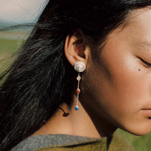 Close-up of woman with dark hair wearing long silver dangle earring with white, red, and blue stones