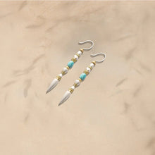 Pair of boho style dangle earrings with white, turquoise, and gold beads on beige background