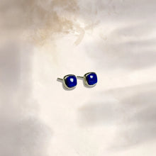 Pair of silver stud earrings with square blue gemstones on a white textured surface