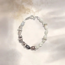 Delicate beaded bracelet with white, gray stones and silver rings on soft fabric background