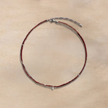 Delicate necklace with small red beads and silver chain on beige surface