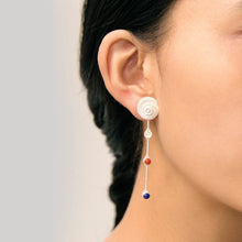 Close-up of ear wearing long silver earring with white spiral top and three colored beads