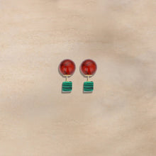 Pair of stylish earrings with red round tops and green striped square drops on beige background